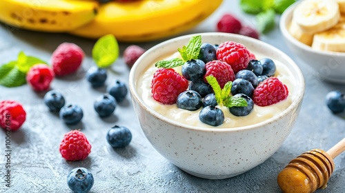 photo of a bowl of yogurt with blue berries, raspberries, peanutbutter, honey, with bananas in the background