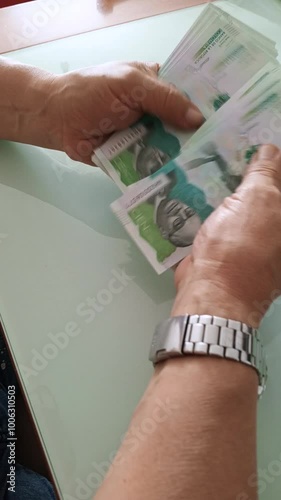 An unrecognizable man counts 100,000 Colombian peso bills on a glass table. Colombian money.