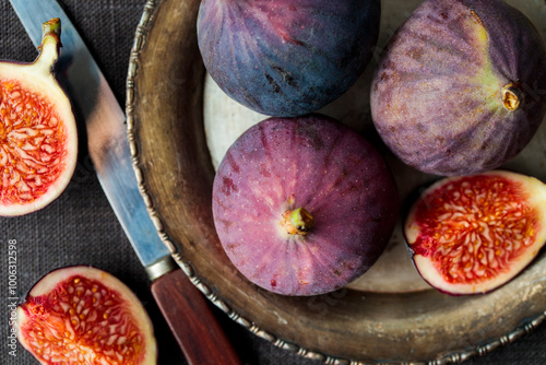Fresh figs on a dark background, whole and sliced ripe, delicious and sweet figs with a kitchen knife on an old rustic metal plate, top view