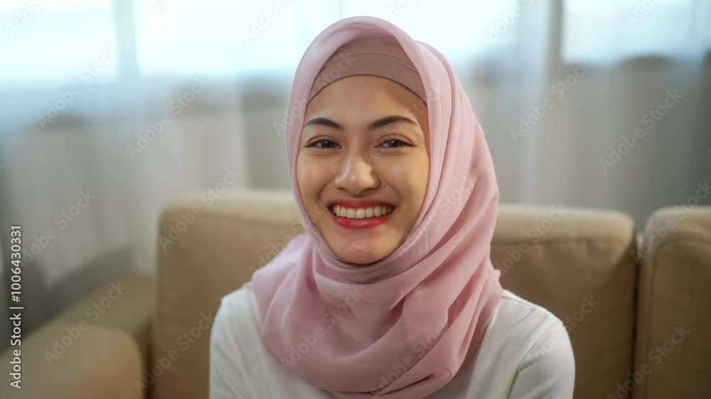 Close up of young beautiful smiling muslim woman in hijab confidently looking at camera in white living room at home, headscarf wearing and stylish asian girl concept.  
