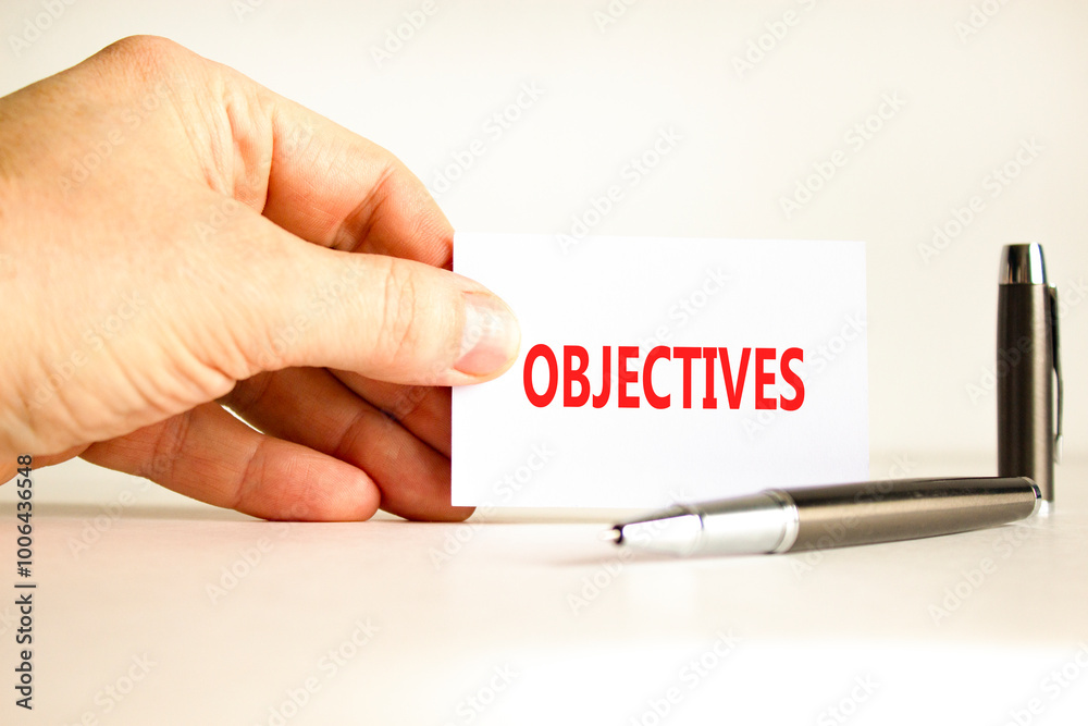 Objectives symbol. Concept word Objectives on beautiful white card. Beautiful wooden background. Businessman hand. Beautiful black pen. Business objectives concept. Copy space. Objectives symbol. Concept word Objectives on beautiful white card. Beautiful wooden background. Businessman hand. Beautiful black pen. Business objectives concept. Copy space.