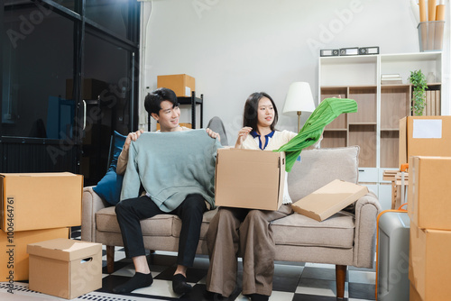 Young couple relaxing sitting on the sofa using the computer laptop around cardboard boxes, very happy moving to a new house.