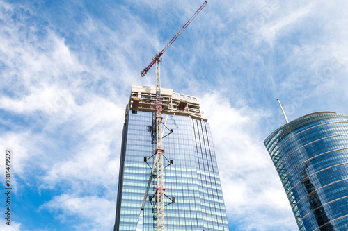 Skyscraper under construction with a crane on a blue sky background.