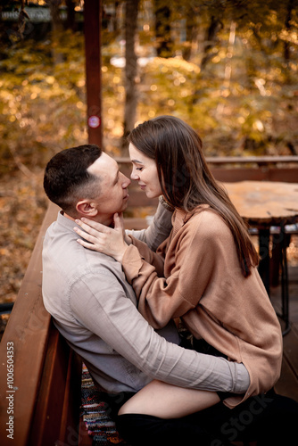 a young couple guy with a girl in autumn in a cafe in brown and orange tones on an outdoor terrace hugging and kissing, love or Valentine's day