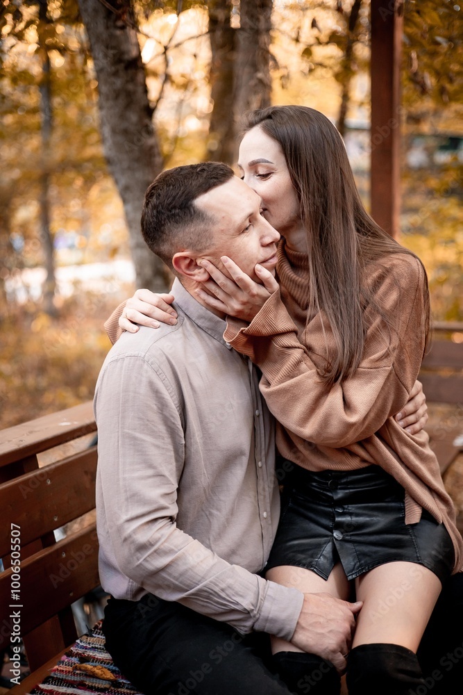 Fototapeta premium a young couple guy with a girl in autumn in a cafe in brown and orange tones on an outdoor terrace hugging and kissing, love or Valentine's day