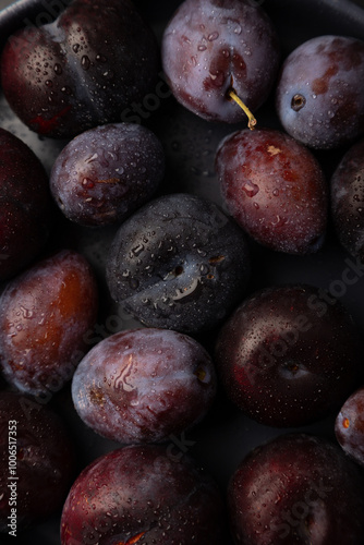 Juicy ripe fresh plum with water drops in gray plate on black background. Seasonal fruits. Selective focus, close-up.