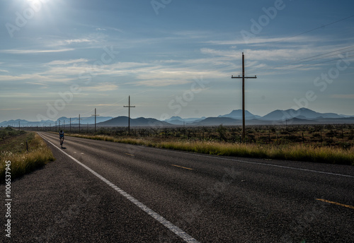 A lone cyclist riding on a straight section of paved road long a desert scene with power line and poles stretching to the horizon, Davis Mountain, Texas