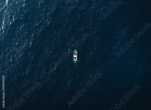 Aerial view of small fishing boat standing in the ocean - horizontal photo. Photo of green boat in the deep ocean water.