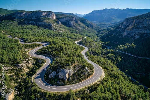 Aerial view of a winding serpentine mountain road navigating through a lush verdant pine forest landscape with a panoramic vista of the surrounding peaks ridges and valleys  This scenic