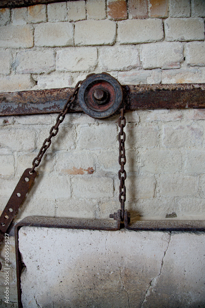 Rusted metal pulley system with chains mounted on a weathered brick wall. The industrial mechanism shows signs of wear and age, adding a vintage, rustic appeal to the structure. Close up image. Rusted metal pulley system with chains mounted on a weathered brick wall. The industrial mechanism shows signs of wear and age, adding a vintage, rustic appeal to the structure. Close up image.