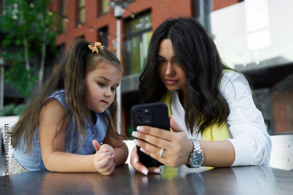 Mother and daughter enjoy time together while looking at a smartphone on a sunny day Mother and daughter enjoy time together while looking at a smartphone on a sunny day