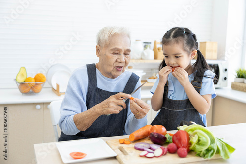 senior woman cutting fresh tomato and vegetables and giving to granddaughter in the kitchen