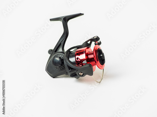 A red and black fishing reel sits on a white background. The reel is small and has a black handle