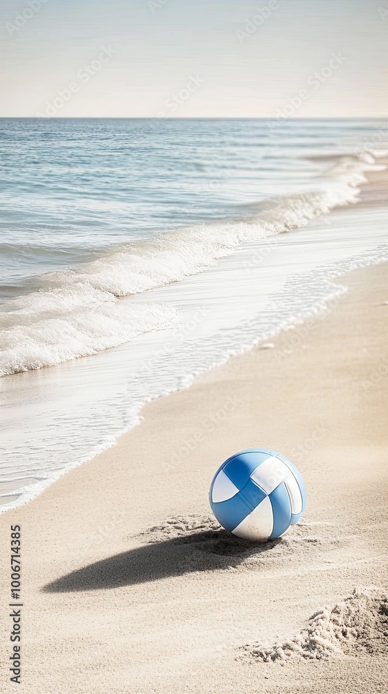Obraz premium A blue and white beach ball sits on a sandy beach, with a view of the ocean behind it.