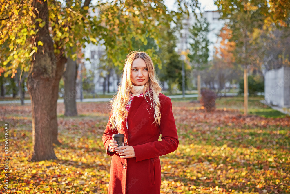 A woman in a red coat and a black skirt walks in an autumn park. The concept of autumn and the beauty of nature. A woman in a red coat and a black skirt walks in an autumn park. The concept of autumn and the beauty of nature.