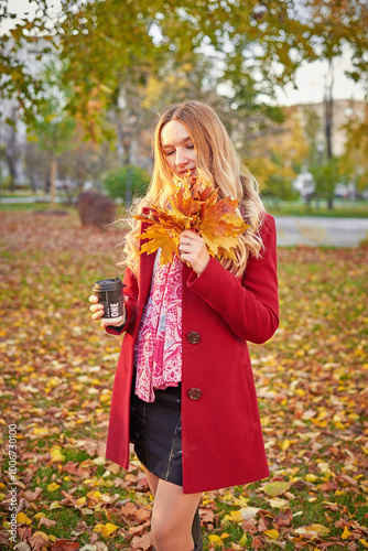 A woman in a red coat and a black skirt walks in an autumn park. The concept of autumn and the beauty of nature.