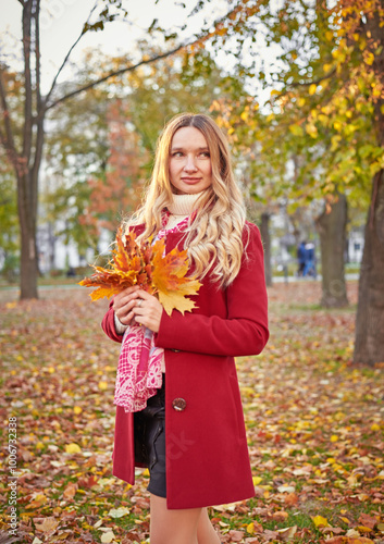 A woman in a red coat and a black skirt walks in an autumn park. The concept of autumn and the beauty of nature.