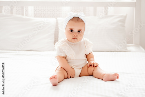 Cute newborn baby girl sitting on a bed in white clothes in a br