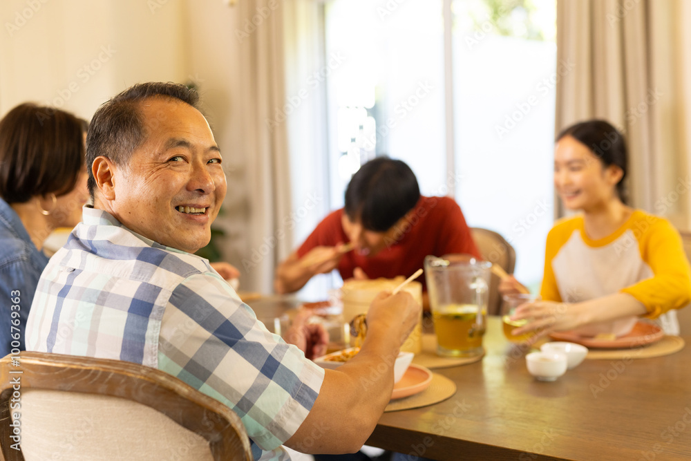 At home, smiling asian man enjoying meal with family, sharing food and conversation at dining table At home, smiling asian man enjoying meal with family, sharing food and conversation at dining table