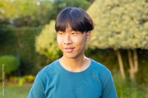 Smiling asian teenage boy in blue shirt enjoying time outdoors in garden