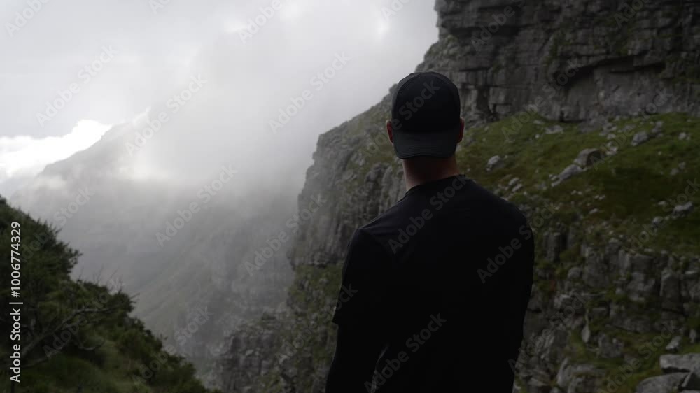 A man shown from behind standing on a mountain and looking out over the misty ridge of the mountains in front of him A man shown from behind standing on a mountain and looking out over the misty ridge of the mountains in front of him