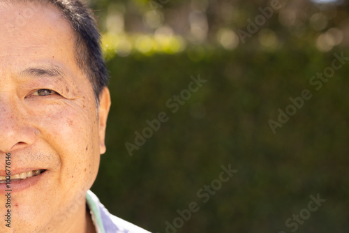 Smiling asian middle-aged man outdoors with greenery in background, enjoying sunny day