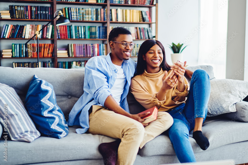 Cheerful African American couple having fun together at cozy living room sitting on sofa with smartphone, young hipster guys taking selfie on mobile phone camera recreating on leisure at home interior Cheerful African American couple having fun together at cozy living room sitting on sofa with smartphone, young hipster guys taking selfie on mobile phone camera recreating on leisure at home interior