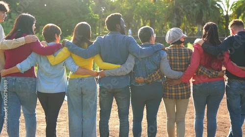 Group of multi generational people having fun hugging each other outdoor - Crowd of multiracial friends enjoy day at city park - Concept of humanity and community