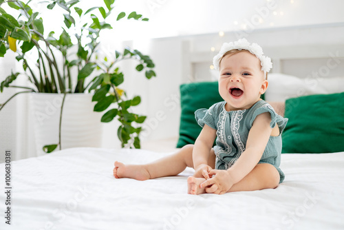 little baby girl on the bed at home in a green bodysuit smiling or laughing, cute funny baby at home before going to bed, lifestyle, photo