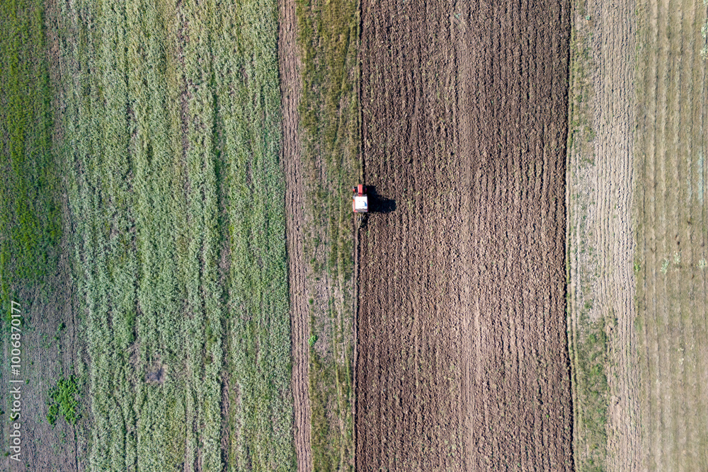 Fototapeta premium Aerial view of a tractor working in a field, showcasing differing soil textures and patterns, emphasizing agricultural productivity.