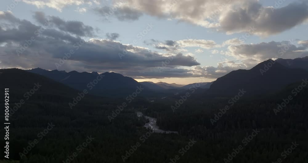 Aerial view of a forested valley with a river winding between mountains at dusk.