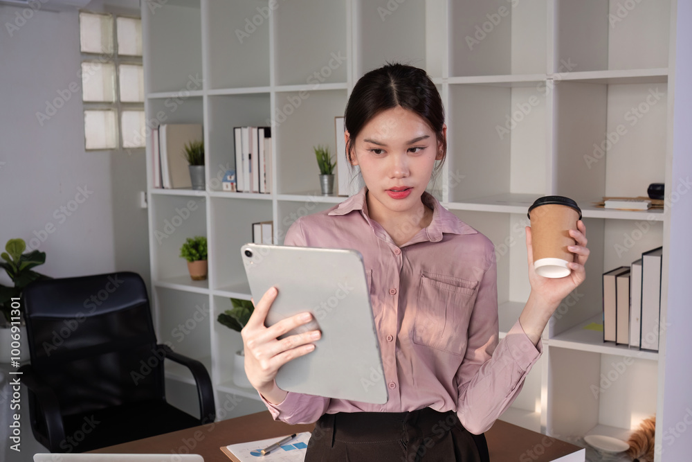 Young Accountant Using Tablet to Communicate with Clients in Modern Office Setting, Holding Coffee Cup