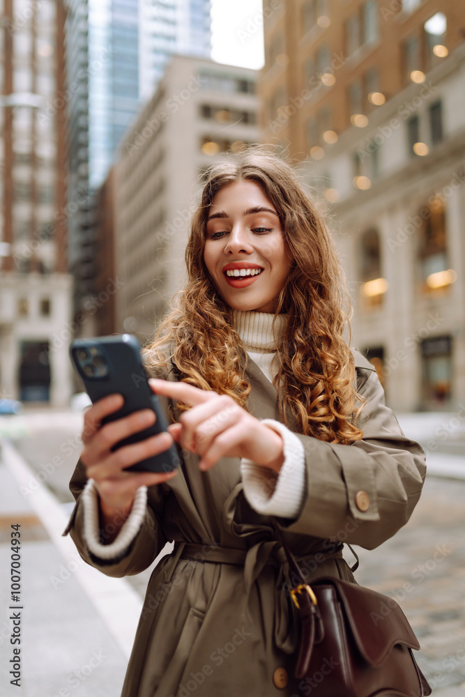 Obraz premium Attractive woman in trench coat using phone outdoor in the street. Lifestyle, travel, tourism, technology