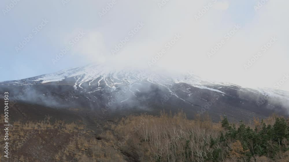 Snow-capped mountain partially covered in mist, with bare trees in foreground. rugged landscape of Fuji mount, featuring snow patches and foggy flow Snow-capped mountain partially covered in mist, with bare trees in foreground. rugged landscape of Fuji mount, featuring snow patches and foggy flow