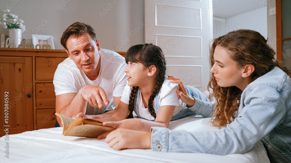 Bedtime story with childhood storytelling, mom and dad reading a fantasy book together to their little young girl in cozy and comfortable bedroom. Modern family happy time. Synchronos Bedtime story with childhood storytelling, mom and dad reading a fantasy book together to their little young girl in cozy and comfortable bedroom. Modern family happy time. Synchronos