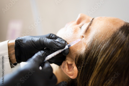 Foto Photograph of the hands of an unrecognizable doctor wearing gloves to inject hyaluronic acid into a woman's crow's feet or contour lines