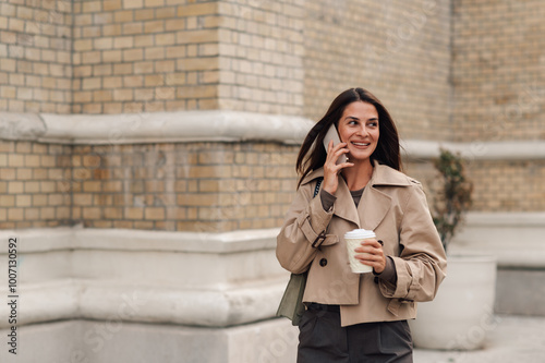 Stylish businesswoman walking and talking on phone with coffee photo