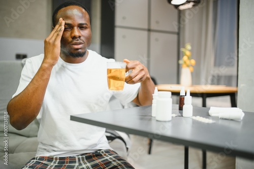 African American man sick with flu or cold at home. He takes medicine and drinks tea