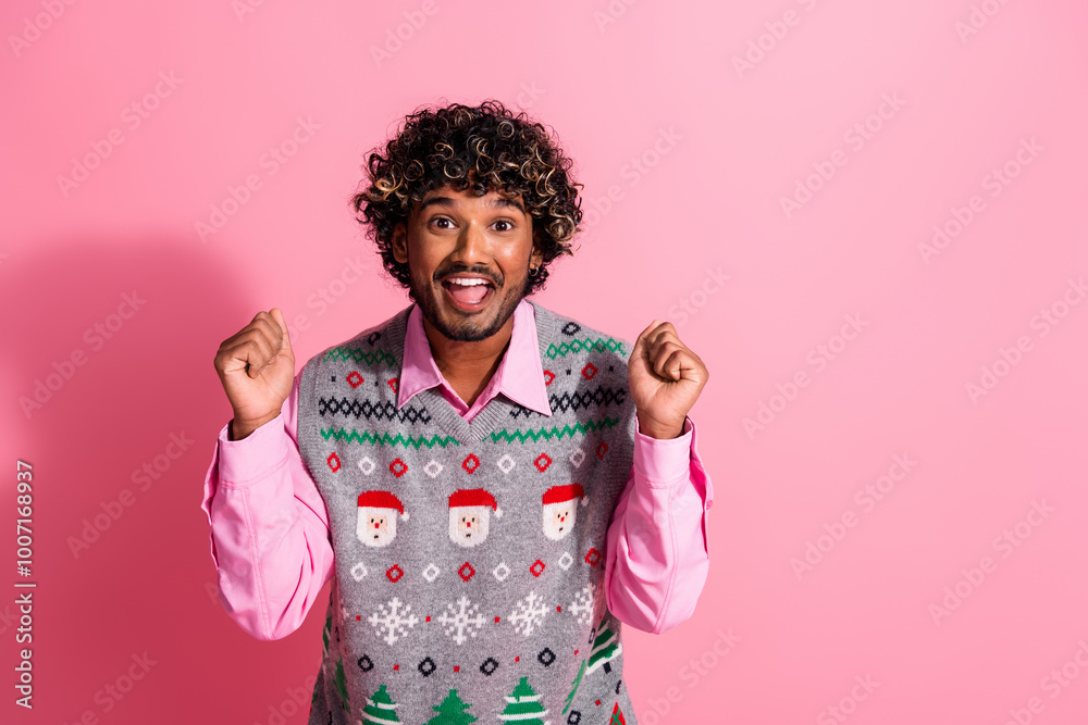 Portrait of nice young man raise fists empty space ad wear new year xmas vest isolated on pink color background Portrait of nice young man raise fists empty space ad wear new year xmas vest isolated on pink color background