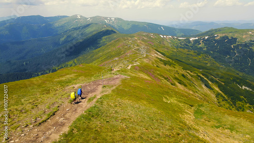 Hikers traversing mountain ridge with expansive views. Two hikers with backpacks traverse a scenic mountain ridge, surrounded by sweeping views of the green hills and distant peaks.