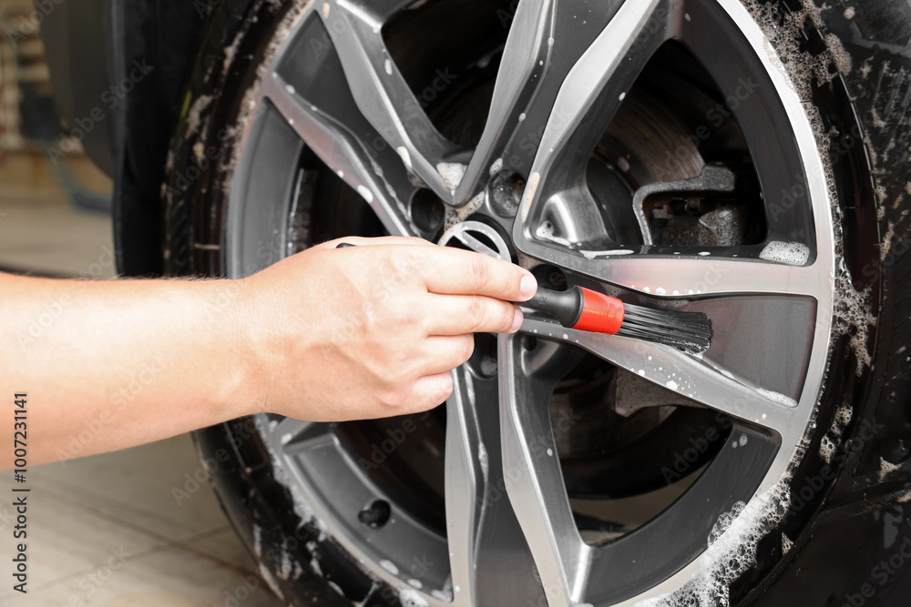 Obraz premium Man cleaning car wheel with brush indoors, closeup