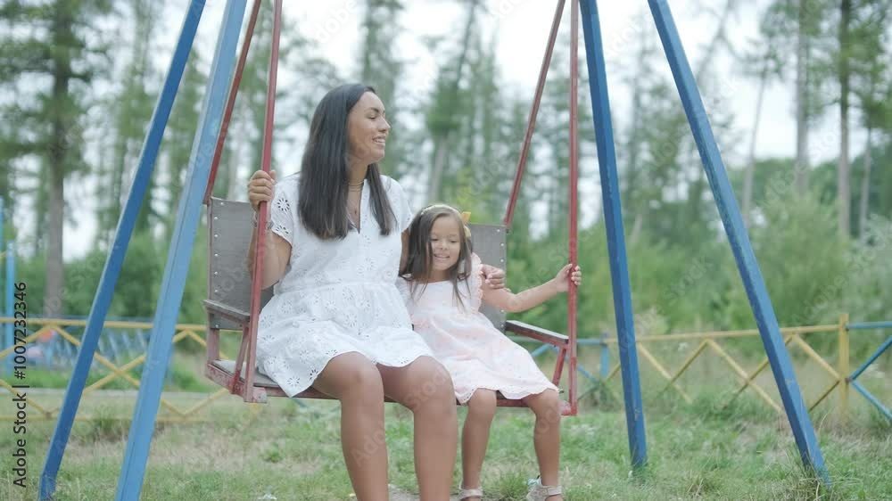 A pregnant mother and her young daughter enjoy playful time together at a playground in the park, surrounded by trees and greenery A pregnant mother and her young daughter enjoy playful time together at a playground in the park, surrounded by trees and greenery