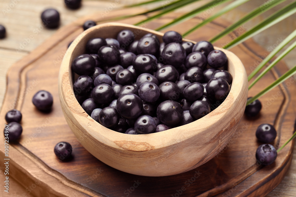 Ripe acai berries in bowl and palm leaves on wooden table, closeup Ripe acai berries in bowl and palm leaves on wooden table, closeup