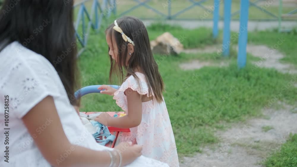 A pregnant mother and her young daughter enjoy playful time together at a playground in the park, surrounded by trees and greenery