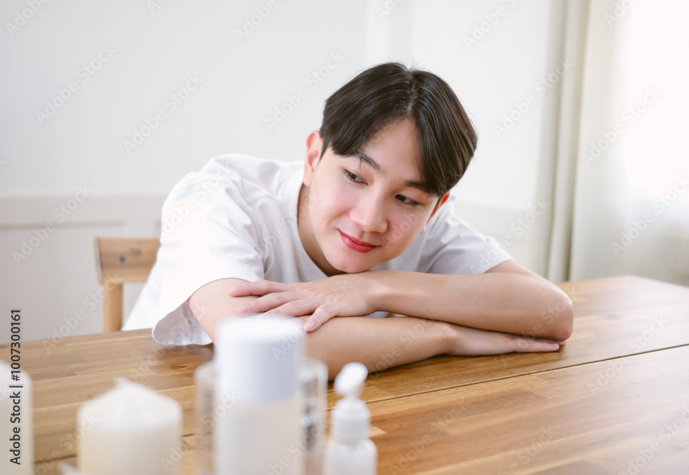 Closeup portrait of inspired caucasian Asian man lying on desk before using moisturizer body oil for beauty treatment, skin care at home. Beauty skincare morning routine concept Closeup portrait of inspired caucasian Asian man lying on desk before using moisturizer body oil for beauty treatment, skin care at home. Beauty skincare morning routine concept