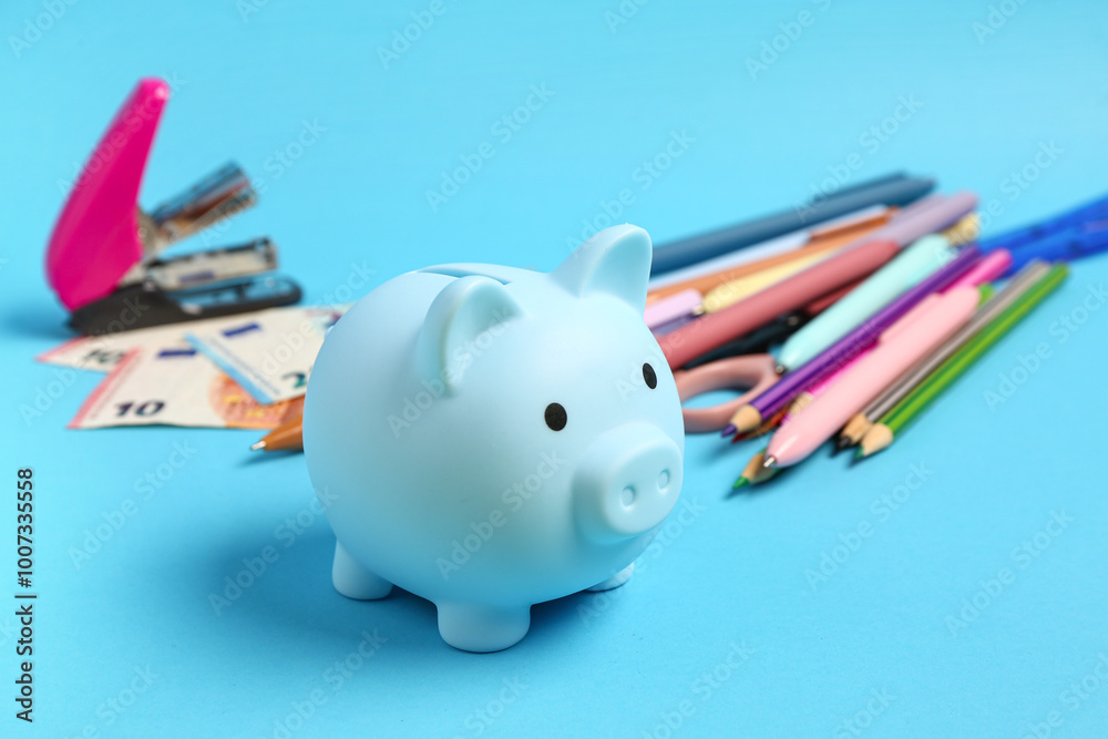 Piggy bank, money and holder with different school stationery on blue background Piggy bank, money and holder with different school stationery on blue background