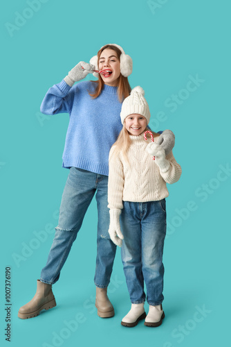 Cute little girl and her mother with Christmas candy canes on blue background