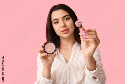 Beautiful young woman with blush and makeup brush on pink background