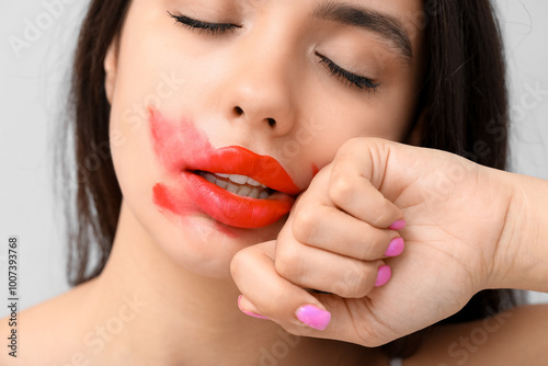 Beautiful young woman with smeared red lipstick on grey background, closeup