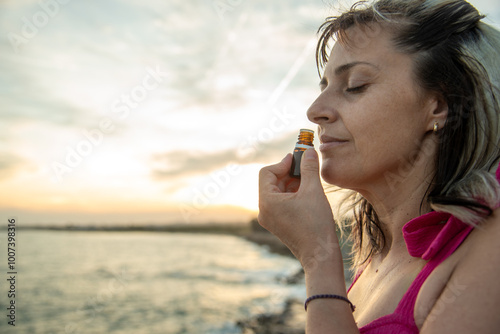woman smelling a bottle of essential oil beside the sea